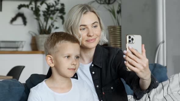 Happy young adult mom teaching little cute kid child son learning using smartphone looking at phone alt