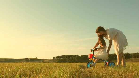 Mom Teaches Daughter To Ride a Bike. Mother Plays with Her Little Daughter alt