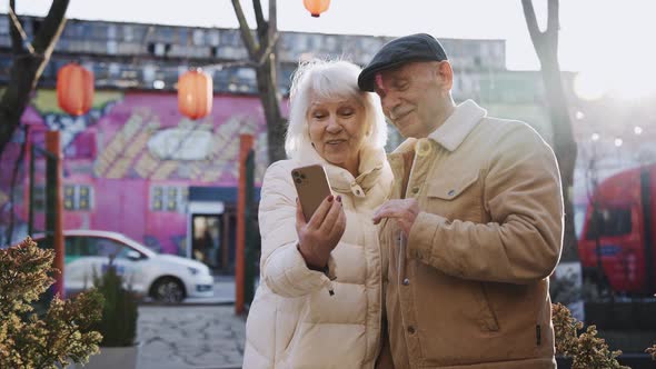 An Elderly Couple Talking on a Video Call Using a Phone Standing on a Street