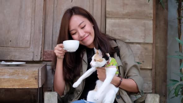 Slow motion of a young asian woman drinking coffee while playing with a little cat