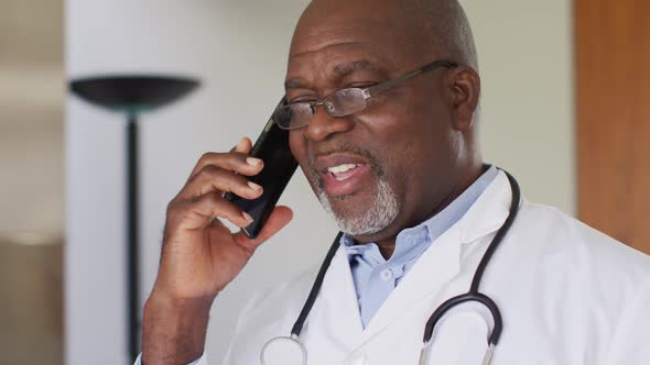 African american senior male doctor wearing white coat talking on smartphone alt