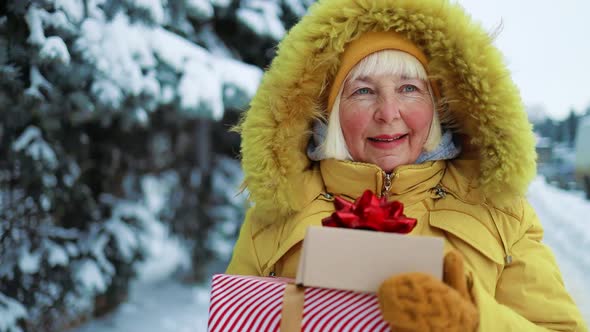 Caucasian Smiling 50s Woman in Yellow Clothes Holds Xmas Present Boxes in Her Hands Over Christmas