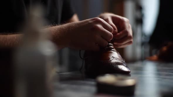 Closeup of Male Shoemaker Tying Laces on Repaired and Polished Light Brown Leather Shoes alt