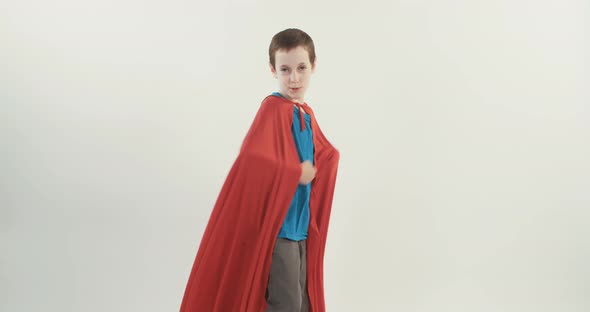 Boy with a superhero cape pretends to fly on a white studio background alt