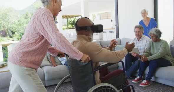 Happy senior diverse people with man in wheelchair using vr headset at retirement home alt