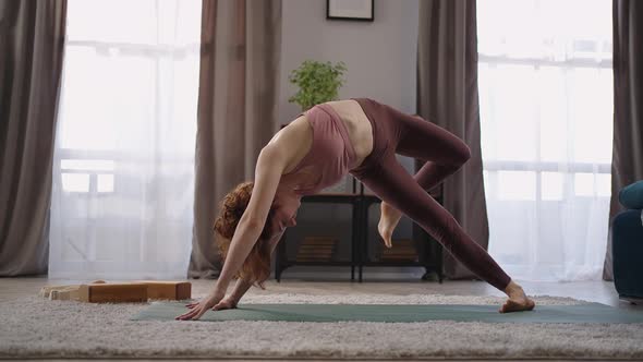 Flexible Trained Woman is Performing Yoga Asanas at Home Standing in Downwardfacing Dog Pose alt