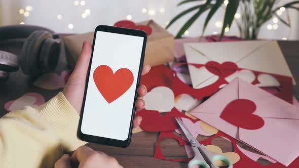 Young Female Hand Holding Smartphone with Red Heart on a Screen alt
