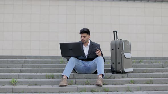 Young Arab Businessman Working on His Laptop Computer While Sitting on the Stairs in the Street with alt