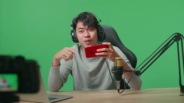 Camera Recording Video Of Asian Man With Headphone Playing Mobile Phone Game On Green Screen alt