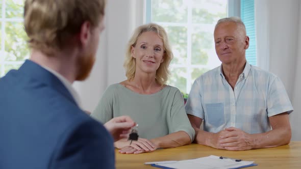 Back View of Real Estate Agent Giving Keys to Senior Couple alt
