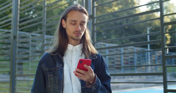 Crop View of Bearded Young Man Using Smartphone While Standing Near Sports Ground. Hipster Guy with alt