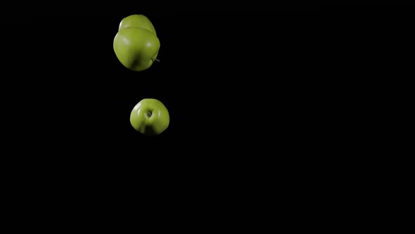 Close Up at the Group of Three Green Apples Fly Up and Spinning on a Black Background in Slow Motion alt