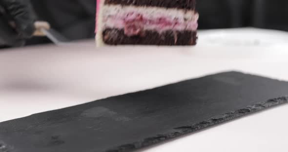 A Closeup of the Hands of a Pastry Chef Placing a Piece of Blueberrygarnished Sponge Cake on a Black
