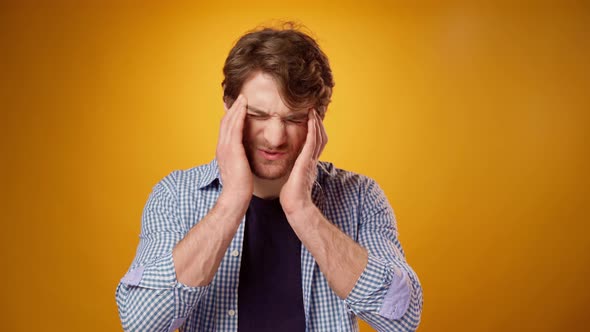 Young Man Suffering From Headache Touching Head Yellow Background alt