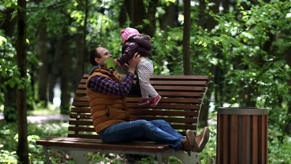 A father and his little daughter are playing on a park bench. Father's day.