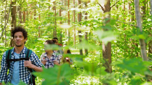 Group of Friends with Backpacks Hiking in Forest alt