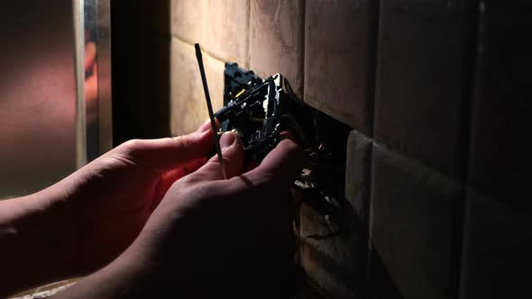 Electrician man repair an electrical outlet socket in apartment in the dark.