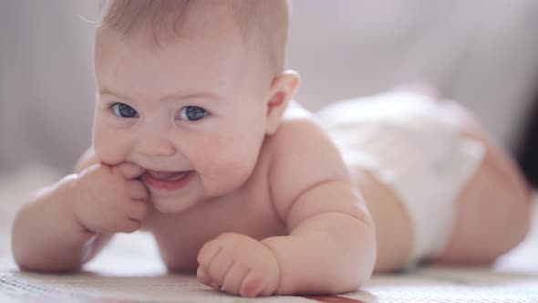 A little baby is lying on his belly against a light background and smiling alt