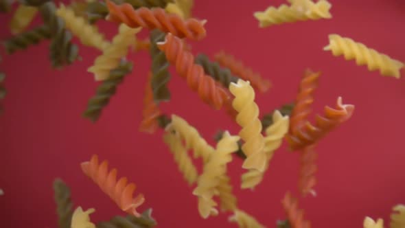 Dry Colored Pasta Fusilli Falling Diagonally on a Wine Red Background alt