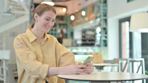 Smiling Young Woman Using Smartphone in Cafe  alt