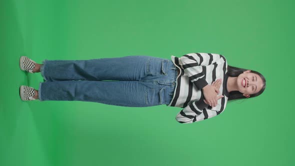 Full Body Of Proud Asian Woman Touching Her Chest While Standing In Front Of Green Screen Background alt
