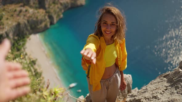 POV Happy Woman Hiker in Yellow Shirt Gives Hand to Her Teammate on Edge of Cliff on Mountain Top alt