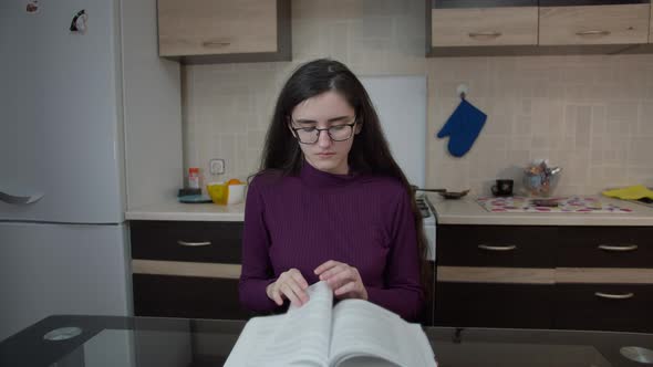Girl Sitting in the Kitchen in the Evening and Studying, School Material on the Book