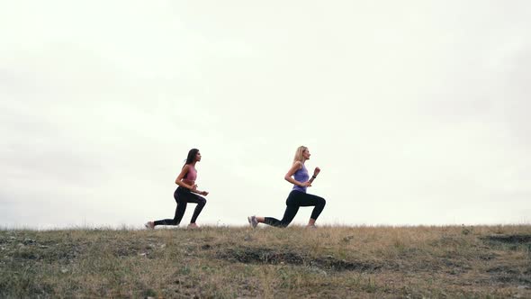 Two Young Athletic Woman in Black Sportswear Stretching Exercises Outdoor on the Sky Background alt
