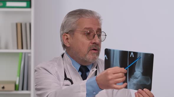 Aged Male Doctor in White Medical Coat Advises Patient By Pointing Out Disease on Picture and alt