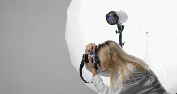 Stylish Young Woman Photographer in a White Shirt with Long Blond Hair Works Making Shots Using