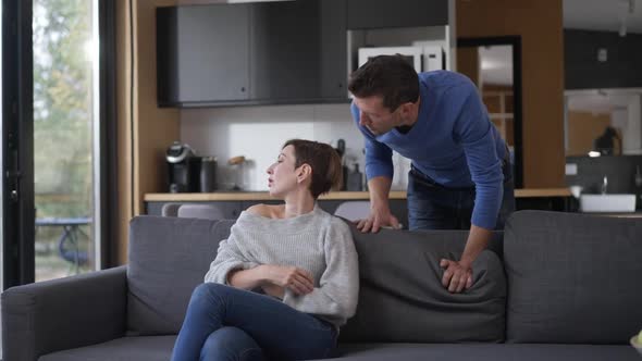 Caucasian Man Talking with Jealous Woman Sitting on Couch in Living Room alt