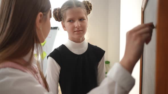 Unsure Girl Shrugging Shoulders As Curios Classmate Talking Writing with Chalk on Blackboard in alt