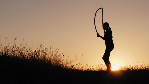 Side View of Training in the Fresh Air  a Silhouette of a Woman Jumping Over a Rope at Sunset alt