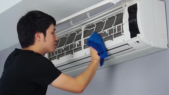 young man cleaning the air conditioner with cloth at home