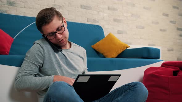 Young Mantalking at the Phone While Write a Message on Laptop Isolated at Home alt