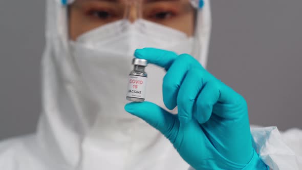 doctor in protective PPE suit holding and gently shaking Coronavirus (Covid-19) vaccine bottle