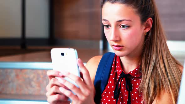 Schoolgirl sitting on staircase and using mobile phone alt