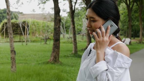 Asian young woman talking on the cell phone while walking on the street at a public park.