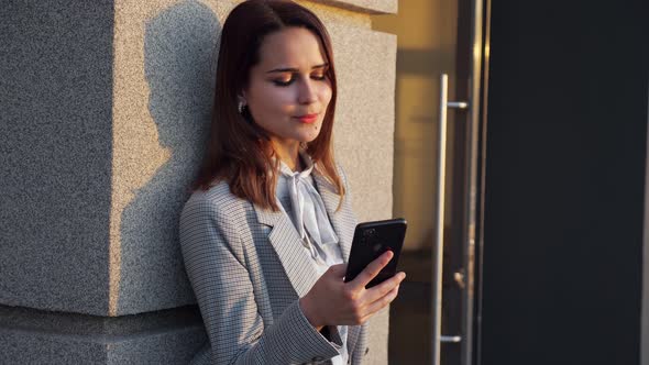 Young Woman in Suit Looking at Phone in Sunlight alt