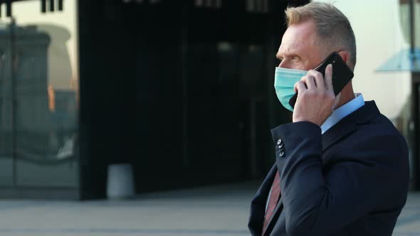 Portrait of Confident Business Man in Blue Medical Mask in Classical Suit Talking on the Phone
