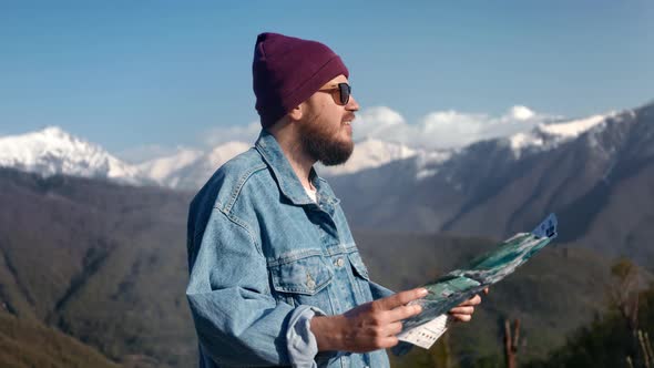 Attractive Traveller Man Hiker with Backpack Checking Map to Find Direction in the Mountains alt