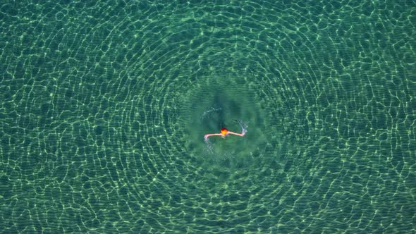 Aerial View a Woman in an Open Clear Transparent Sea is Spinning Creating Round Waves Around Her a alt