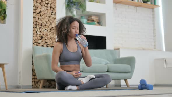 African Woman Drinking Water While Doing Yoga at Home alt