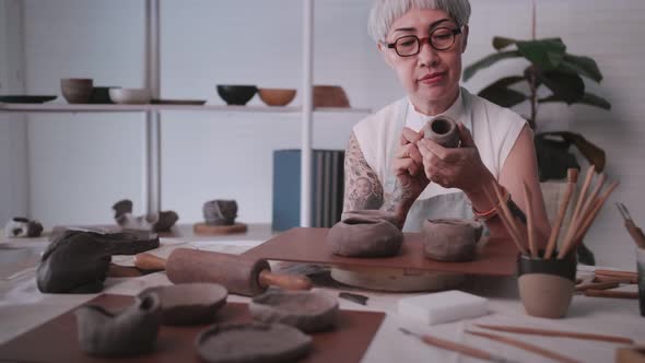 Asian elderly woman enjoying pottery work at home. alt