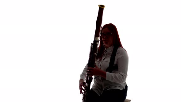 Silhouette Woman Plays Bassoon Music Sitting on Chair in Studio White Background Front View alt