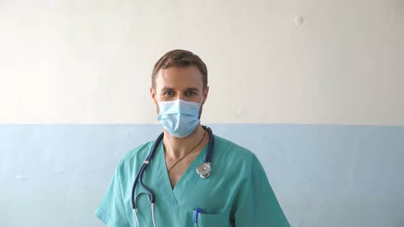 Portrait of Young Male Caucasian Doctor with Medical Face Mask Looks at Camera alt