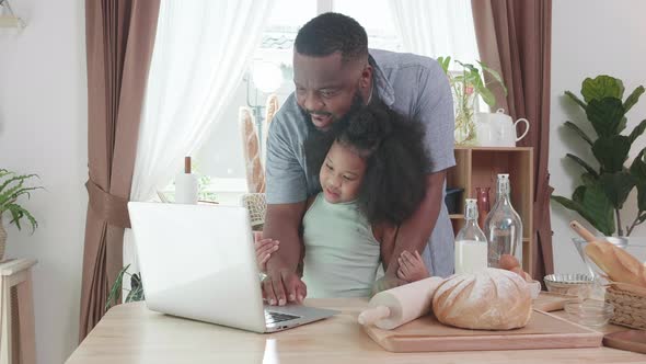 Happy African American family daughter and her father using laptop together at kitchen table