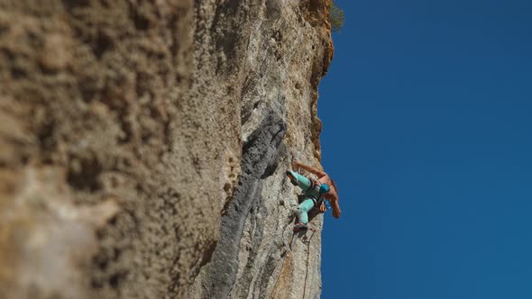 Bottom View of Muscular Strong Man Rock Climber Climbs on Vertical Cliff on Rock Wall on Blue Sky alt