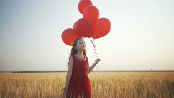 Happy Young Girl with Balloons Running in the Wheat Field at Sunset alt