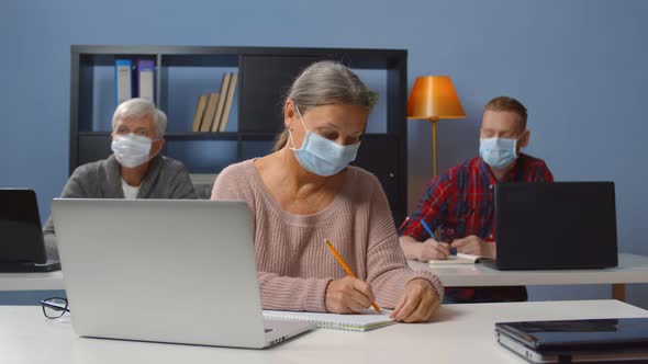 Group of Adult Students Wearing Safety Mask Sitting in Classroom alt